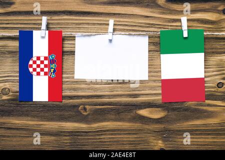 Hanging flags of Croatia and Italy attached to rope with clothes pins with copy space on white note paper on wooden background.Diplomatic relations be Stock Photo