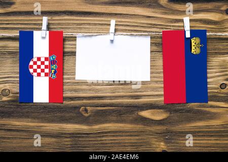 Hanging flags of Croatia and Liechtenstein attached to rope with clothes pins with copy space on white note paper on wooden background.Diplomatic rela Stock Photo