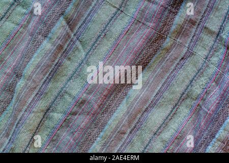 The texture of the fabric with multi-colored stripes on the diagonal. A lot of stitches on the fabric. Crumpled fabric. Red, green, brown colors. Stock Photo