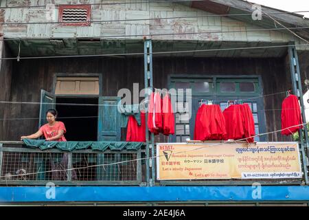 A mature Burmese woman hangs red & green sports uniforms out to dry on clotheslines as part of her laundry business in Homalin, Myanmar (Burma) Stock Photo