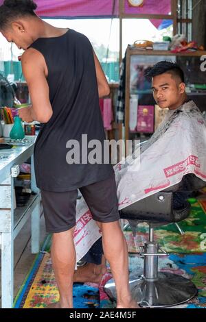 Barber cuts the hair of a younger male client in a makeshift barber shop in Homalin in northwestern Myanmar (Burma) along the Chindwin River Stock Photo