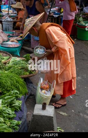 A Buddhist monk shops in the railroad marketplace on the tracks of a local railroad with  stalls, vendors and umbrellas in Mandalay, Myanmar (Burma) Stock Photo