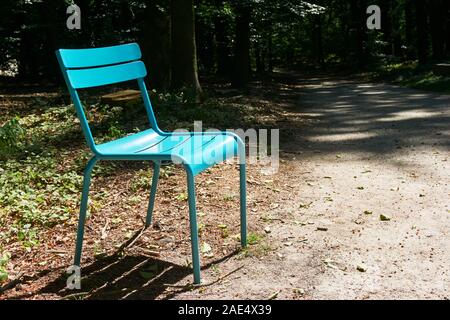 Modern sun-lit blue green shiny plastic chair in dark forest with copy space Stock Photo