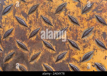 Close-up of old weathered rusty brown industrial anti slip metal plate with diamond pattern and worn yellow paint Stock Photo
