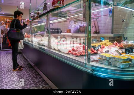 A female customer waits at the counter of a meat butcher shop as the clerk fills her order in Nice, France. Stock Photo