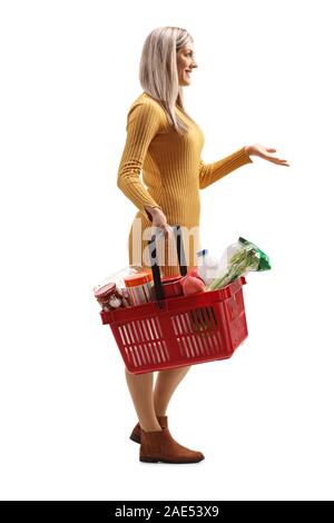 Full length profile shot of a young woman carrying a full shopping basket and gesturing with hand isolated on white background Stock Photo