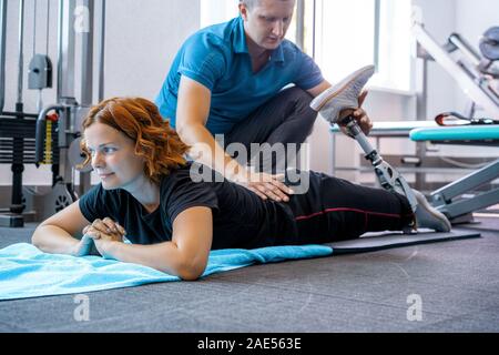 Personal trainer assisting woman with disabilities in her workout. Sports Rehab Centre with physiotherapists and patients working together towards hea Stock Photo