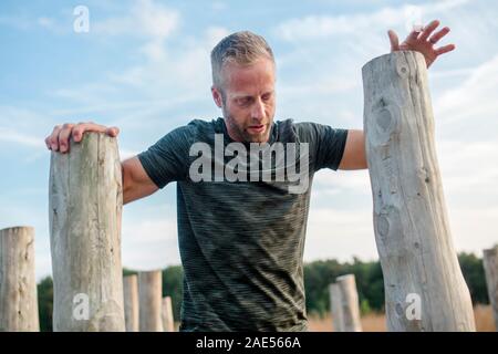 Top-half of man leaning on wood poles on obstacle course Stock Photo