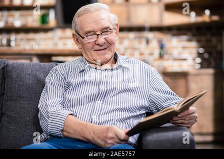 Cheerful aged man in glasses reading a book Stock Photo