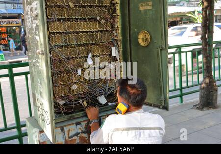 Bangkok, Thailand - December 4, 2019 : A technician sitting on sidewalk inspecting telephone lines inside the telephone exchange box Stock Photo