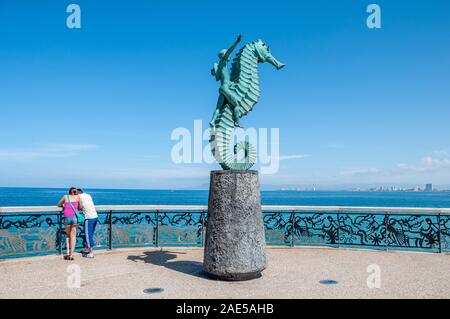 A tourist couple  stands by the famous Cabellero del Mar landmark sculpture on the Puerto Vallarta malecon. Stock Photo