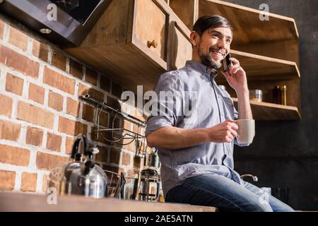 Positive man talking on phone in the kitchen Stock Photo
