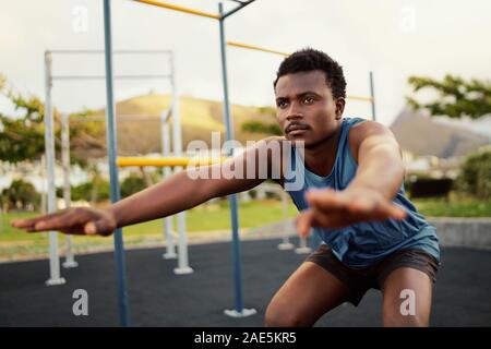 Athletic young man in sportswear doing physical exercises at outdoor gym park - young african american man doing squats Stock Photo
