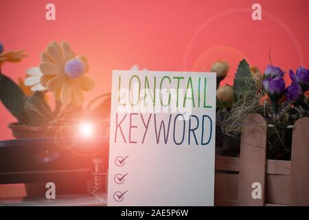 Writing note showing Longtail Keyword. Business concept for search phrases that are highly relevant to specific niche Flowers and writing equipments p Stock Photo