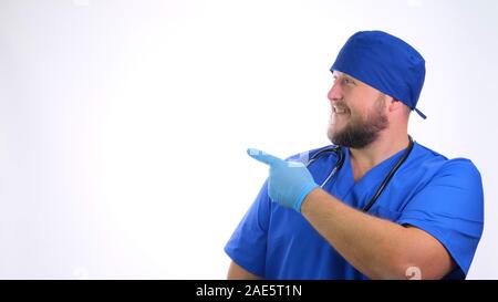 bearded smiling doctor man in blue uniform shows his hand on a blank space on a white background. Stock Photo