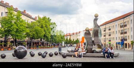 People sitting on edge of modern bronze and plastic sculpture and fountain in markltplatz  Dessau Saxony-Anhalt Germany. Stock Photo