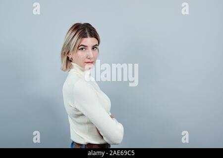 Smiling woman in casual clothes holding hands crossed, isolated on gray wall Stock Photo