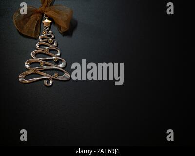 Stylized silver Christmas tree with gold toned ornaments, star, and bow against a black background. Stock Photo