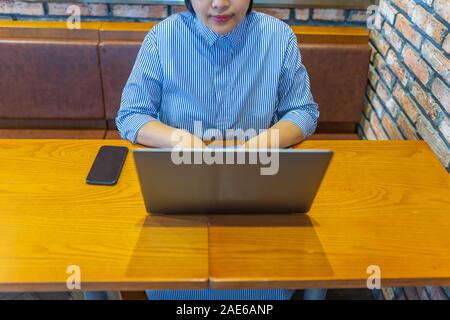 Asian businesswoman working on laptop beside smartphone on wooden table Stock Photo