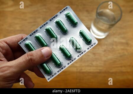 Photo of hand holding a foil pack filled with herbal cough medicine and glass water on a wooden table Stock Photo