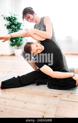 Young man doing yoga with woman trainer in gym against background of window with green flower Stock Photo
