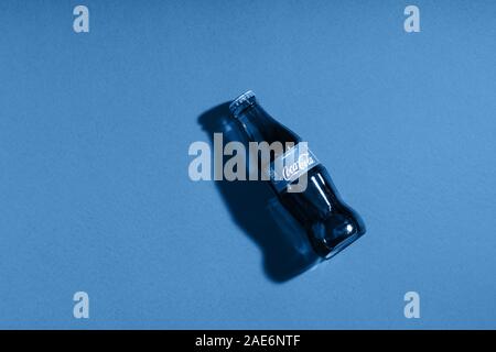 Coca Cola in glass bottle on blue paper background. Trendy color of the year 2020. Italy, Milan - 15 November 2019 Stock Photo