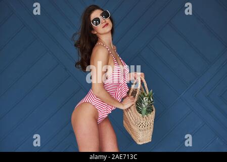 Cheerful young woman going to the sea. Stylish beautiful young girl in bikini stands and posing in the studio Stock Photo