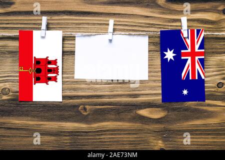 Hanging flags of Gibraltar and Heard and Mcdonald Islands attached to rope with clothes pins with copy space on white note paper on wooden background. Stock Photo