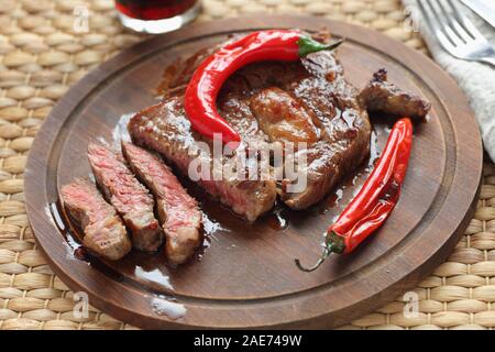 Sliced medium rare beef steak topped with roasted chili pepper on a wooden cutting board Stock Photo