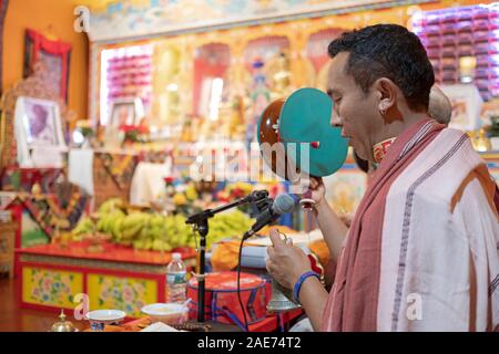 With the altar as a backdrop, a Buddhist monk plays the damaru drums at a monthly Throma Puja at a temple in Elmhurst, Queens, New York City. Stock Photo