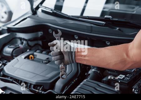 Man's hand in glove holds wrench in front of broken automobile Stock Photo