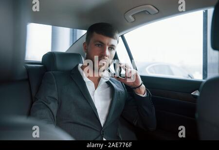Mature adult. Businessman in official wear have call when sitting on the back of car Stock Photo
