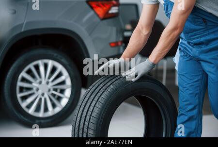 Rolling it on the floor. Mechanic holding a tire at the repair garage. Replacement of winter and summer tires Stock Photo