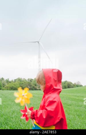 Boy with two pinwheels in front of wind farm. Stock Photo