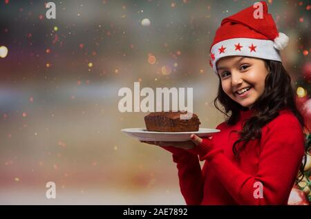 Portrait of a young girl holding a plate of rum cake in hand during Christmas. Stock Photo