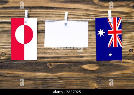 Hanging flags of Greenland and Heard and Mcdonald Islands attached to rope with clothes pins with copy space on white note paper on wooden background. Stock Photo