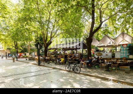 Tirana, Albania, July 8 2019: People walking at a pedestrian city street with trees in Tirana, people at a outdoor cafe on the side. Stock Photo