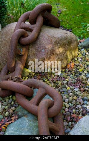 Ship rusty chain resting on stones. Symbol of strength, security and safety. A green lawn in the background, a chain out of focus in the foreground. Stock Photo