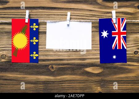 Hanging flags of Guadeloupe and Heard and Mcdonald Islands attached to rope with clothes pins with copy space on white note paper on wooden background Stock Photo