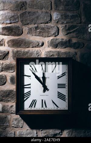 Square clock hanging on a stone wall. Stock Photo
