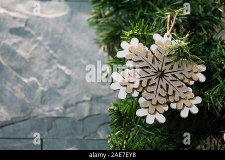 Christmas fir tree branches decorated with wooden figure of snowflake. Copy space for text. Gray stone wall background. Bright festive holiday decorat Stock Photo