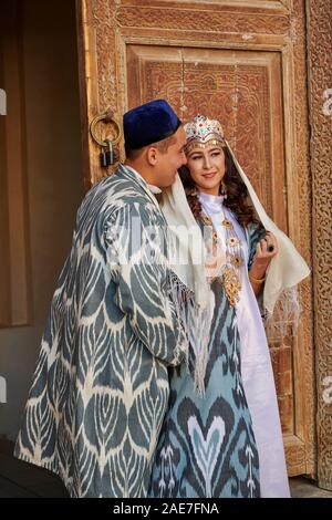 bridal couple in traditional clothes posing in front of famous Registan Square, Samarkand, Uzbekistan, Central Asia Stock Photo