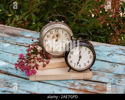 Time concept. Two old clock and old books on rustic wooden table. Outdoor Stock Photo