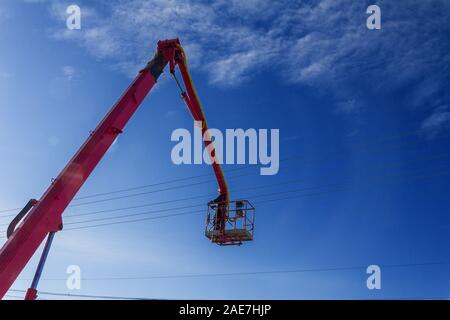 working electrician working at height on hydraulic aerial platform against the blue sky Stock Photo