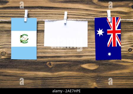 Hanging flags of Guatemala and Heard and Mcdonald Islands attached to rope with clothes pins with copy space on white note paper on wooden background. Stock Photo