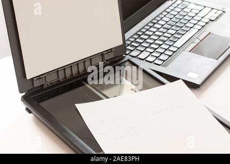 Open flatbed scanner with paper lying on it and a notebook computer in background. Selective focos image. Stock Photo