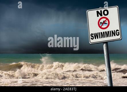 No swimming. Danger sign at the beach with a rough sea with rainy sky on background Stock Photo