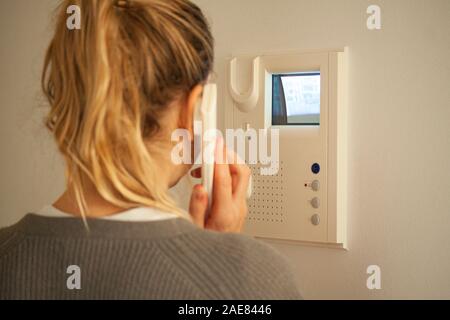 Blonde woman answering a call at a door phone while looking at the screen on the CRT display. Video intercom equipment. Selective focus image. Stock Photo