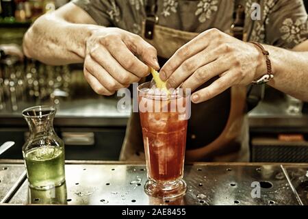 Bartender is adding lemon zest to the cocktail at bar counter, toned image Stock Photo