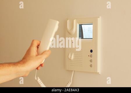Video door phone with image on CRT display hanging on a wall. Hand holding handset. Video intercom equipment.  Selective focus image. Stock Photo